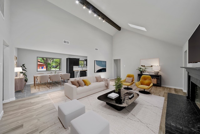 living room with beamed ceiling, high vaulted ceiling, light wood-style flooring, visible vents, and a brick fireplace