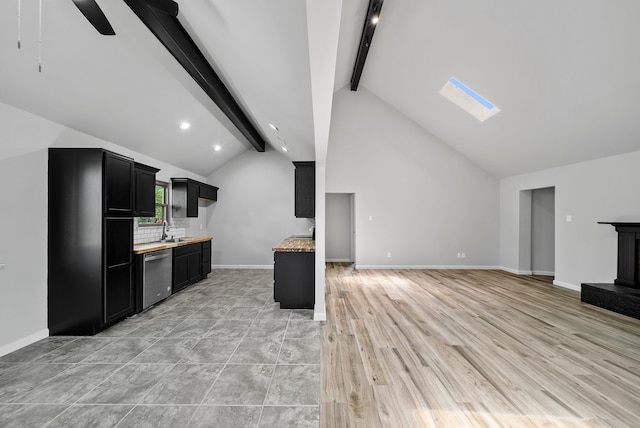 kitchen featuring dark cabinets, open floor plan, lofted ceiling with skylight, stainless steel dishwasher, and a sink