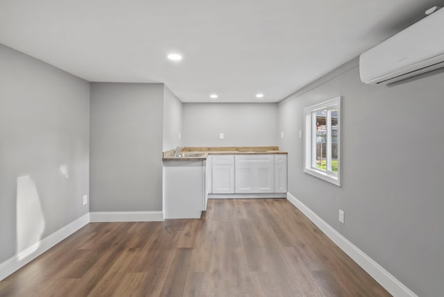 kitchen featuring baseboards, an AC wall unit, recessed lighting, wood finished floors, and white cabinets