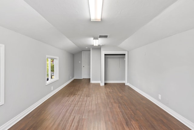 unfurnished bedroom with wood finished floors, visible vents, baseboards, lofted ceiling, and a closet