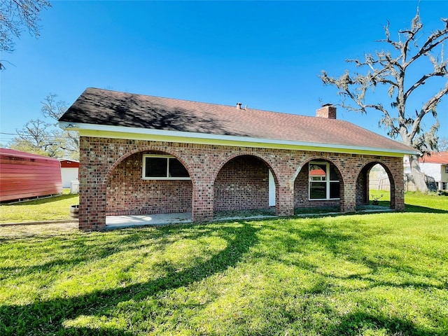view of front of home with brick siding, a front yard, roof with shingles, and a chimney