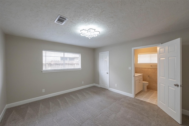 9315 Fairdale Ln, Houston, TX 77063 - unfurnished bedroom featuring light carpet, multiple windows, a textured ceiling, ensuite bath, and baseboards