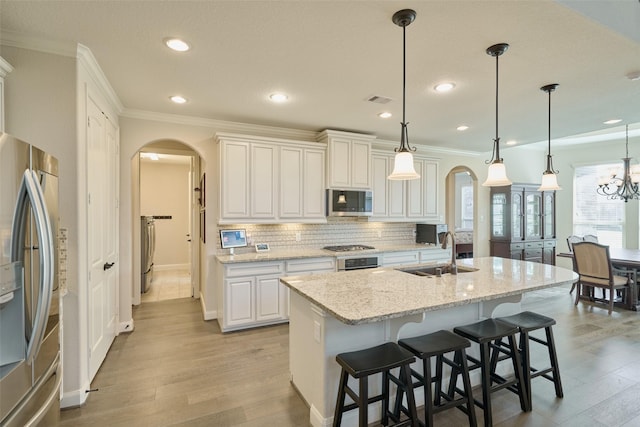 120 Shane St, Montgomery, TX 77316 - kitchen featuring arched walkways, appliances with stainless steel finishes, a sink, light wood-type flooring, and crown molding