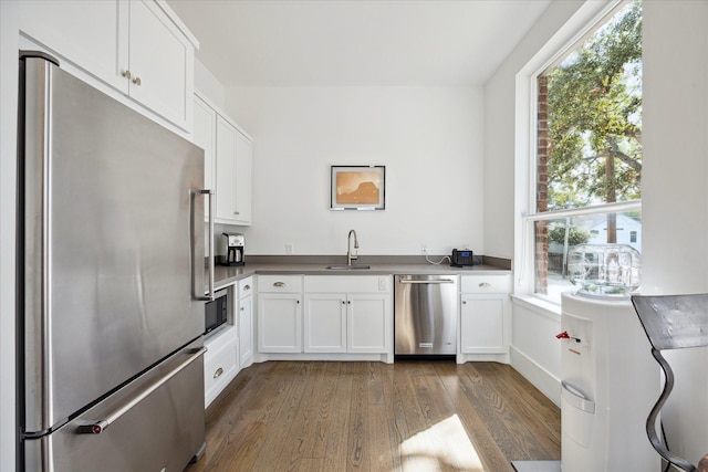 kitchen with a sink, wood-type flooring, white cabinets, and stainless steel appliances