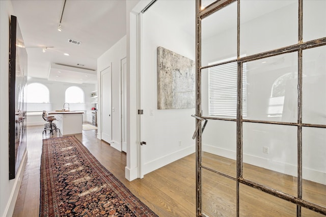 hall featuring baseboards, light wood-type flooring, a sink, and visible vents