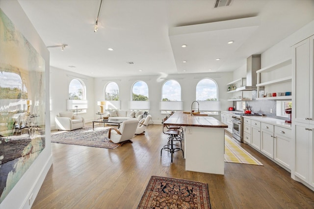 kitchen with high end stainless steel range, wall chimney exhaust hood, white cabinetry, a breakfast bar, and a center island with sink