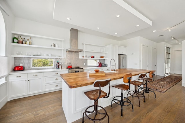 kitchen featuring wall chimney range hood, freestanding refrigerator, open shelves, stove, and a sink