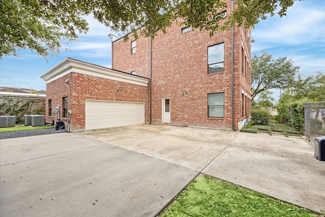 view of side of property with a garage, fence, brick siding, concrete driveway, and central AC unit