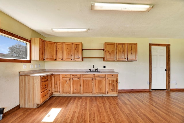 kitchen featuring open shelves, light countertops, a sink, light wood-type flooring, and baseboards