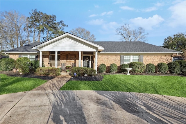view of front of property with a front yard, brick siding, covered porch, and roof with shingles
