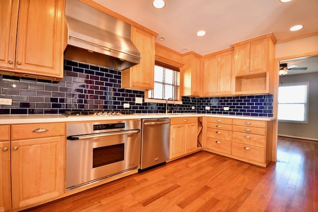 kitchen with light wood-style flooring, wall chimney range hood, light brown cabinetry, and appliances with stainless steel finishes
