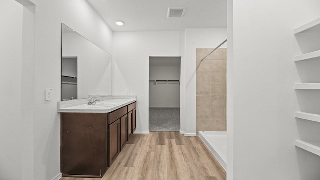full bath featuring a tile shower, vanity, a spacious closet, visible vents, and wood finished floors
