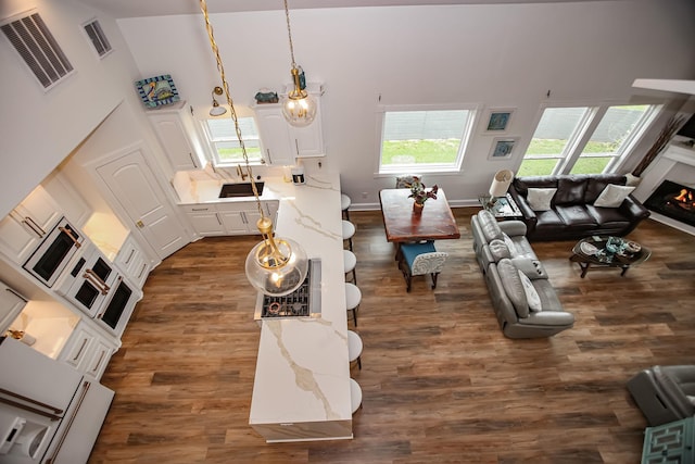 living area featuring dark wood finished floors, a warm lit fireplace, visible vents, and a towering ceiling