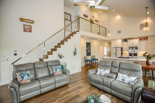 living room with visible vents, a ceiling fan, wood finished floors, and a towering ceiling