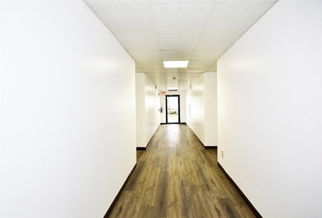 hall featuring dark wood-style flooring, baseboards, and a drop ceiling