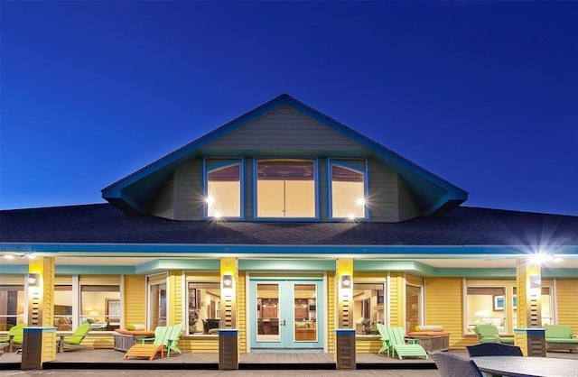 back of house at night with french doors, an outdoor hangout area, and roof with shingles