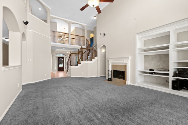 unfurnished living room featuring carpet flooring, built in shelves, arched walkways, ceiling fan, and a fireplace
