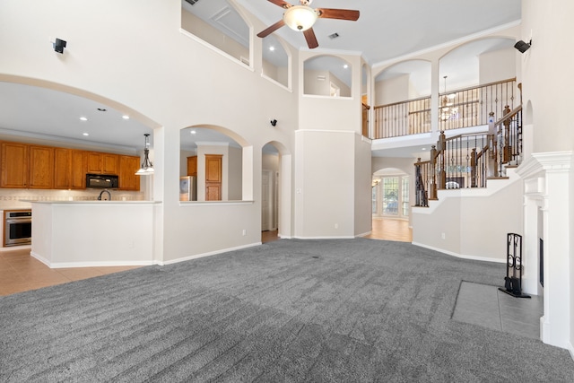 unfurnished living room with stairs, crown molding, a ceiling fan, light colored carpet, and arched walkways