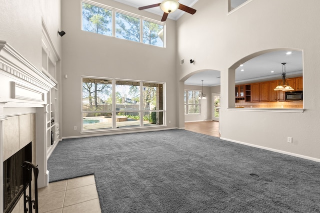 unfurnished living room with light carpet, baseboards, arched walkways, and a ceiling fan