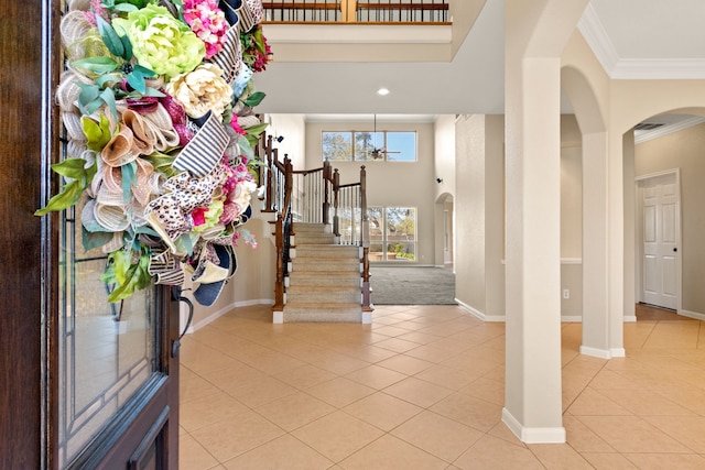 foyer entrance with arched walkways, light tile patterned floors, a towering ceiling, and crown molding