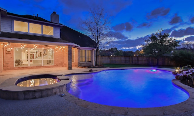 pool at dusk with a patio, fence, and a pool with connected hot tub