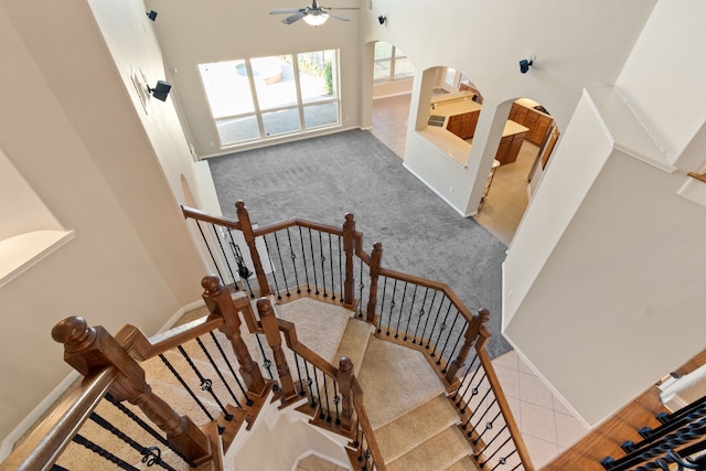 stairs featuring a towering ceiling, tile patterned flooring, baseboards, arched walkways, and ceiling fan