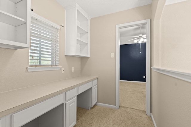 unfurnished office with built in study area, a ceiling fan, light carpet, and baseboards
