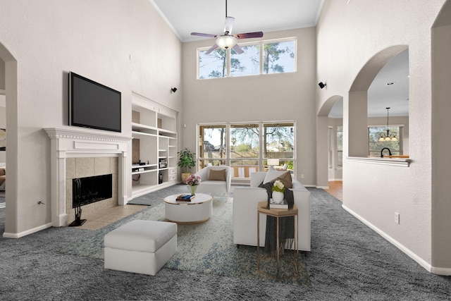 carpeted living area featuring crown molding, arched walkways, ceiling fan, and a tile fireplace