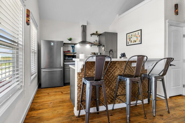 1072 Johnson Rd, Gilchrist, TX 77617 - kitchen featuring freestanding refrigerator, wall chimney range hood, a kitchen breakfast bar, lofted ceiling, and healthy amount of natural light