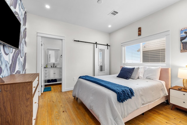 1072 Johnson Rd, Gilchrist, TX 77617 - bedroom with a barn door, light wood-type flooring, recessed lighting, a sink, and ensuite bath