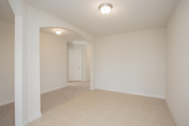 spare room featuring arched walkways, light colored carpet, and baseboards