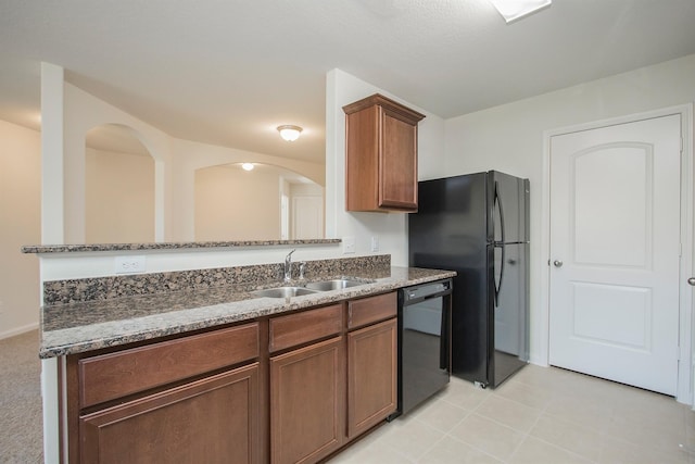 kitchen with black appliances, dark stone countertops, brown cabinetry, and a sink