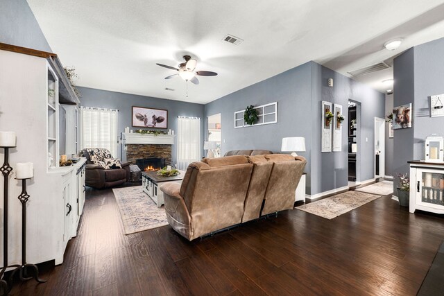 living area featuring dark wood-style flooring, baseboards, a stone fireplace, a ceiling fan, and visible vents