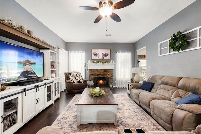 living area featuring dark wood-type flooring, ceiling fan, a fireplace, and visible vents