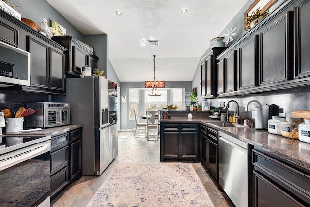 kitchen with a sink, dark countertops, vaulted ceiling, and stainless steel appliances