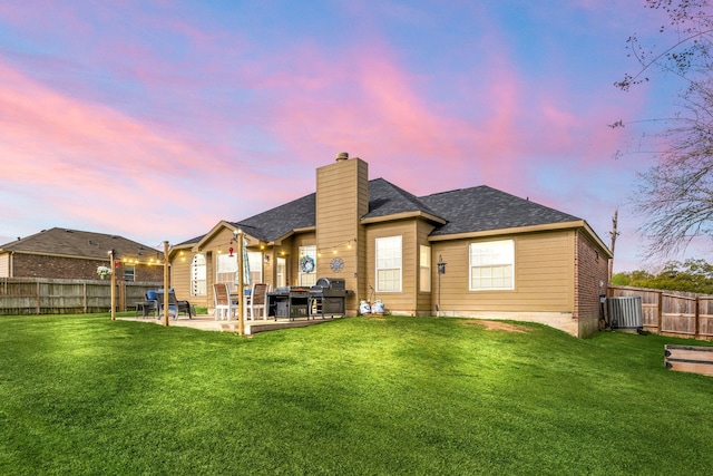 back of house at dusk with a chimney, a patio area, a fenced backyard, and a lawn