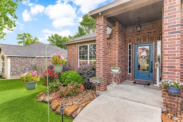 doorway to property with roof with shingles, a yard, and brick siding