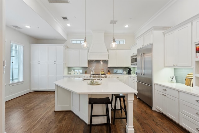 kitchen featuring custom exhaust hood, a center island with sink, visible vents, and built in appliances