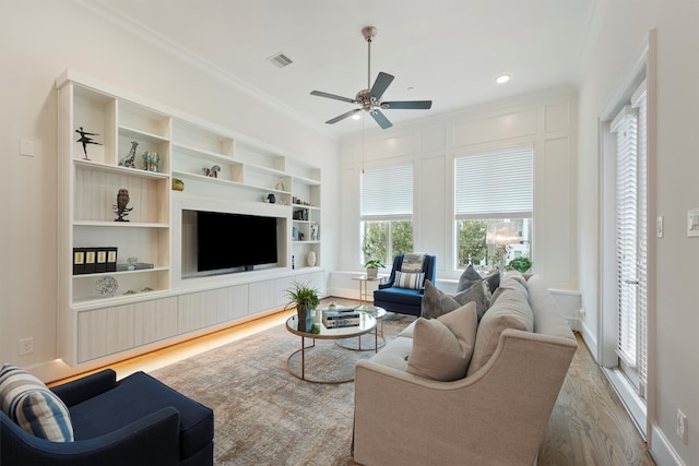 living area featuring visible vents, built in shelves, wood finished floors, ceiling fan, and crown molding