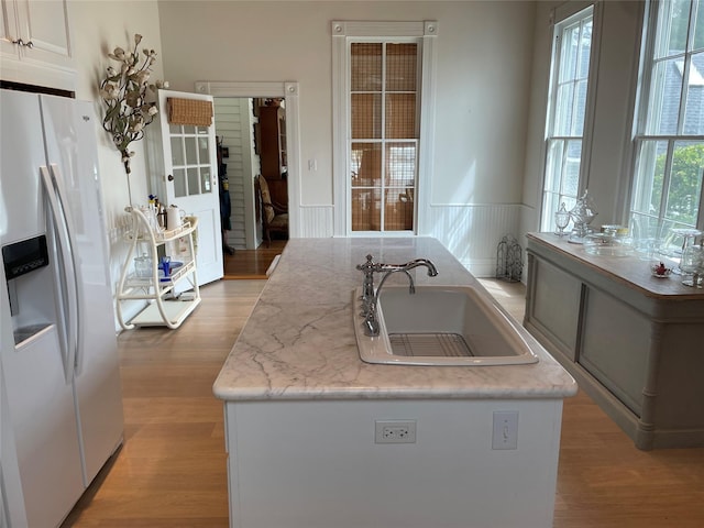 kitchen with a wainscoted wall, light wood-type flooring, white refrigerator with ice dispenser, white cabinetry, and a sink