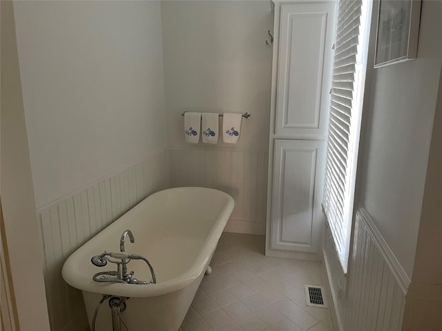 bathroom with a wainscoted wall, a soaking tub, visible vents, and tile patterned flooring