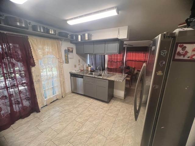 kitchen featuring stainless steel appliances, a sink, light stone countertops, and gray cabinetry