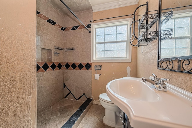 bathroom with toilet, ornamental molding, a sink, tiled shower, and a textured wall