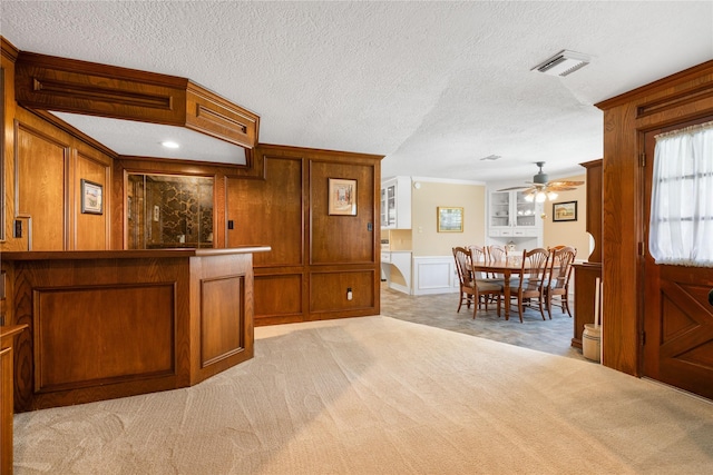 kitchen featuring ceiling fan, brown cabinetry, a decorative wall, and light carpet