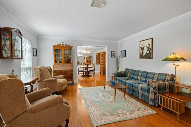 living room with an inviting chandelier, a textured ceiling, wood finished floors, visible vents, and ornamental molding