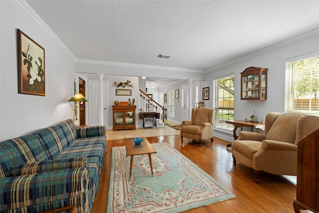 living area with a healthy amount of sunlight, ornamental molding, decorative columns, and light wood-type flooring