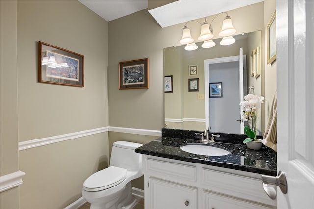 half bathroom with toilet, a skylight, baseboards, and vanity