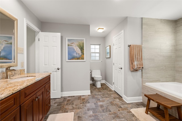 full bath with vanity, toilet, baseboards, a tub, and stone finish flooring