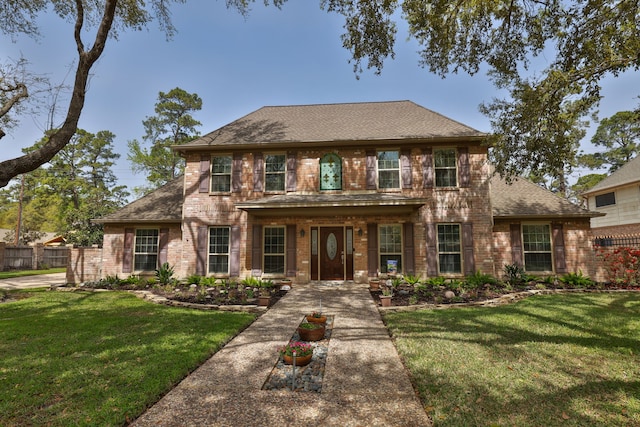 view of front of house featuring brick siding, fence, a front yard, and roof with shingles