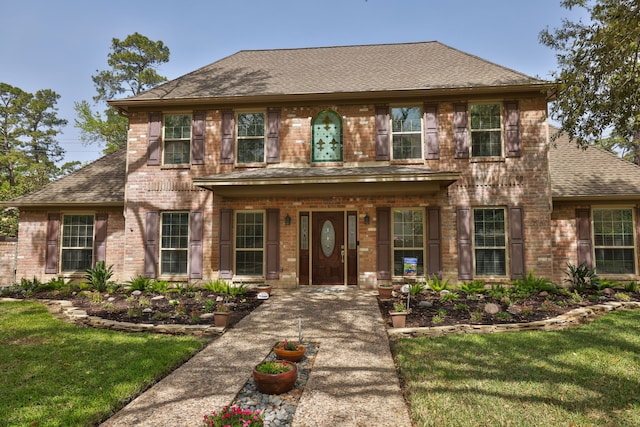 view of front facade featuring brick siding, a shingled roof, a front lawn, and a porch